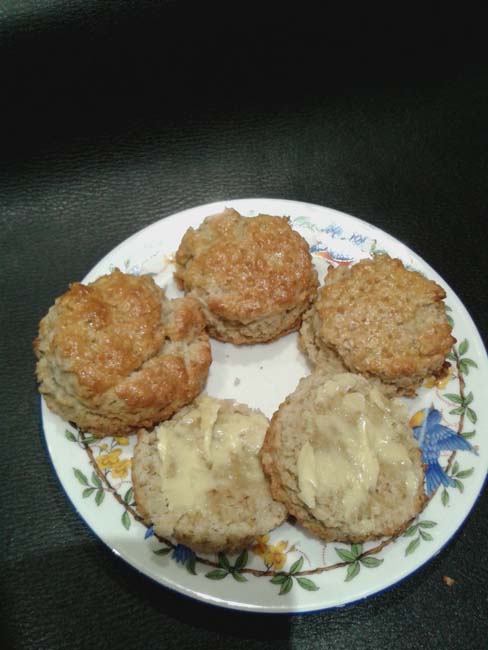 Four scones on a china plate, one cut in half and nicely spread with oozing butter. The scone must be warm!